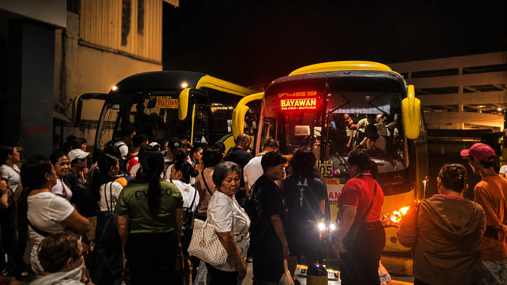 Riders waiting to board a night coach at a Ceres terminal, destination board lit for Bayawan
